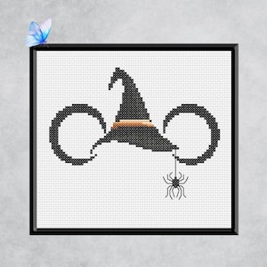 May include: Cross-stitch design featuring a black witch's hat with a brown band, two black circular shapes, and a hanging spider. The design is framed in black and set against a white background, perfect for Halloween decor.