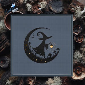 Puede incluir: Arte de punto de cruz enmarcado que representa una silueta negra de bruja sobre una luna creciente, sosteniendo una linterna. El diseño incluye estrellas y setas, con el texto "Enchant Stitch".
