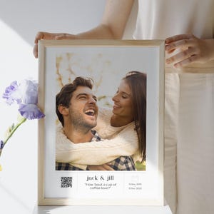 Puede incluir: Una foto enmarcada de una pareja, Jack & Jill, sonriendo y riendo. La foto está en un marco de madera claro y tiene un passe-partout blanco. El texto "How 'bout a cup of coffee love?" está impreso debajo de la foto, junto con un código QR.