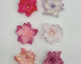 May include: Six fabric flower embellishments arranged in two columns. The left column features Passion Fruit, Pink, and Rose Pink flowers. The right column features Lilac, Lt. Pink, and Rosy Mauve flowers. Each flower has a central bead accent.