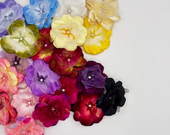 May include: A collection of layered fabric flowers in various colors including blue, white, yellow, green, purple, pink, red, and black. Each flower features delicate petals and a small, sparkling rhinestone or beaded center detail.