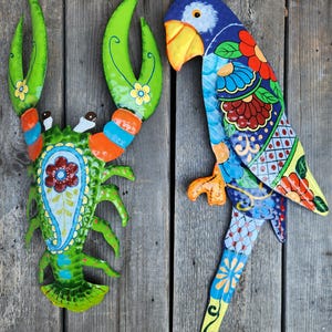 May include: A colourful metal lobster and parrot wall decor. The lobster is green, orange, and blue with a paisley design. The parrot is blue, yellow, red, and green with a floral design.