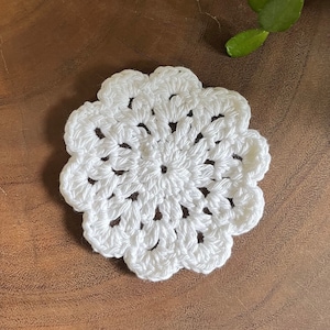 Puede incluir: Posavasos de ganchillo blanco con un diseño circular. El posavasos está hecho de hilo blanco y tiene un patrón delicado y de encaje.