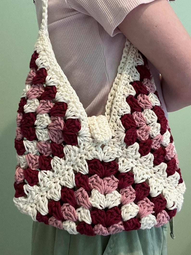 Puede incluir: Bolso de crochet hecho a mano con dise&ntilde;o de granny square. El bolso est&aacute; hecho con hilo crema, burdeos y rosa. La correa y el cierre son de color crema. El bolso es un bolso de hombro.