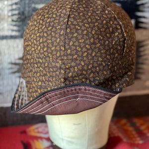 May include: A brown and gold patterned fabric hat with a brown brim. The hat is turned inside out to show the brown fabric lining.