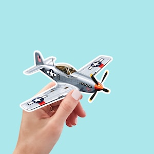May include: A silver and red paper airplane with a blue and white star on the wing. The airplane is held in a hand.