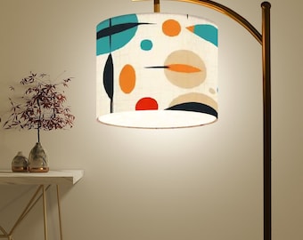 May include: A gold floor lamp with a curved arm and a white drum lampshade with a colourful abstract pattern of blue, orange, and red circles and lines.