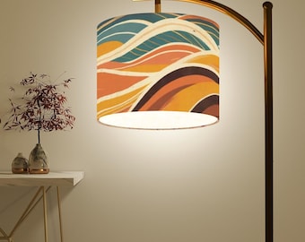 May include: A gold floor lamp with a curved arm and a white drum lampshade with a colourful abstract pattern of orange, brown, and blue waves.