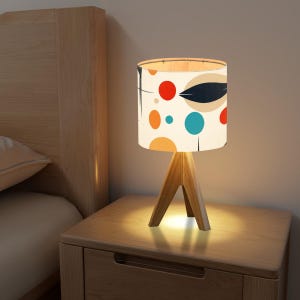 May include: A wooden table lamp with a white lampshade featuring a colorful abstract design of circles and a leaf. The lampshade has a white background with orange, red, blue, and black accents.