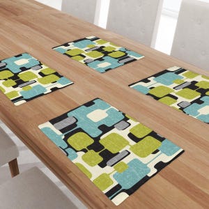 May include: Four rectangular placemats with a retro design. The placemats feature a pattern of overlapping shapes in teal, lime green, grey, black, and white. They are arranged on a light brown wooden table.