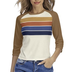 May include: A three-quarter sleeve baseball style shirt. The shirt has brown sleeves and a cream-colored body with horizontal stripes in shades of gold, rust, blue, and navy. The shirt is made of a soft, comfortable material.