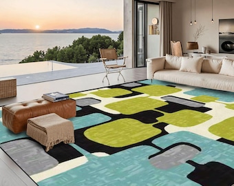 May include: A large area rug with a mid-century modern design. The rug features a pattern of overlapping shapes in shades of green, blue, black, gray, and white. The rug is placed in a living room with a view of the ocean.