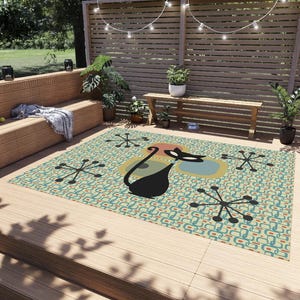 May include: A black cat silhouette with a retro mid-century modern design on a teal, yellow, and orange outdoor rug. The rug has a repeating pattern of circles and stars.