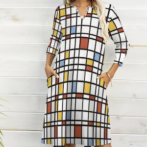 May include: A white dress with a geometric pattern of red, yellow, and blue squares. The dress has a v-neck and 3/4 sleeves. It has two pockets on the sides.