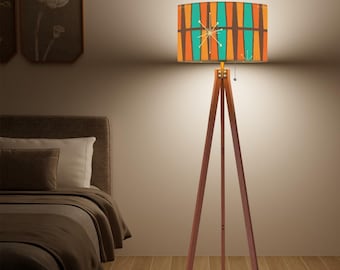 May include: A mid-century modern style floor lamp with a wooden tripod base. The lampshade features a colorful geometric pattern in orange, teal, and brown. A starburst design is centered on the shade. The lamp is a stylish addition to any room.