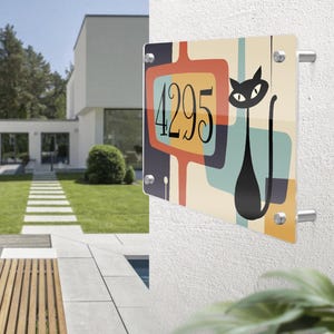 May include: A colorful house number sign with a black cat silhouette and the number 4295. The sign has a retro, mid-century modern design with geometric shapes in shades of blue, yellow, orange, and cream.