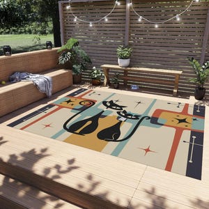 May include: A retro-style outdoor rug with a beige background and a colourful geometric pattern. Two black cats with white accents are featured in the centre of the rug.