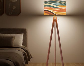 May include: A wooden tripod floor lamp with a rectangular lampshade. The lampshade features a colorful abstract design with horizontal lines in shades of blue, orange, and brown. The lamp is in a bedroom setting.