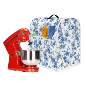 Puede incluir: Una batidora de pie roja con un cuenco y un accesorio de batidor de acero inoxidable. Junto a ella, una funda blanca con un estampado floral azul, con bolsillos que contienen una espátula, un pincel y otros utensilios de cocina. La funda tiene un asa negra.