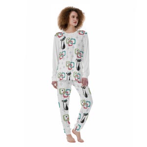 Puede incluir: Conjunto de pijama blanco con un patrón repetido de siluetas de gatos negros y formas geométricas coloridas. La parte superior de manga larga y los pantalones presentan un diseño retro con acentos rojos, verdes y azules. El pijama está hecho de un material suave y cómodo.