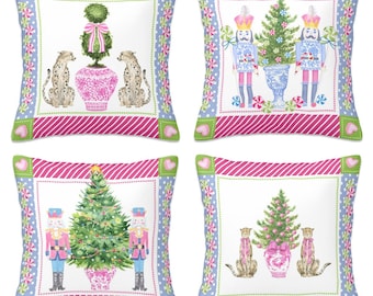 Puede incluir: Cuatro cojines decorativos con varios diseños. Uno presenta un topiario y guepardos, otro tiene cascanueces y un árbol de Navidad, y los otros tienen temas similares. Cada cojín tiene un centro blanco con un borde rosa y azul.