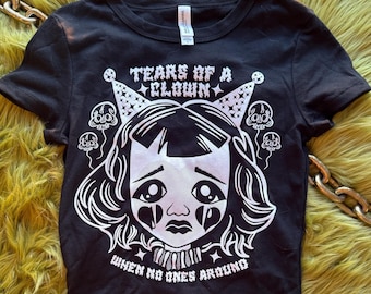 May include: Black cropped t-shirt with a white graphic of a sad clown with the text "Tears of a Clown When No Ones Around".