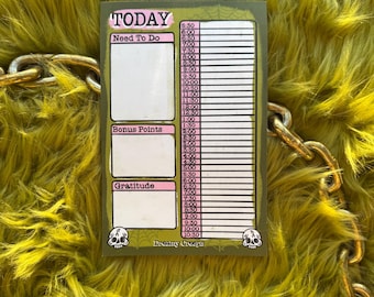 May include: A pink and green daily planner with the words "TODAY", "Need To Do", "Bonus Points", and "Gratitude" printed on it. The planner has a skull graphic and the text "Dreamy Creeps" at the bottom.