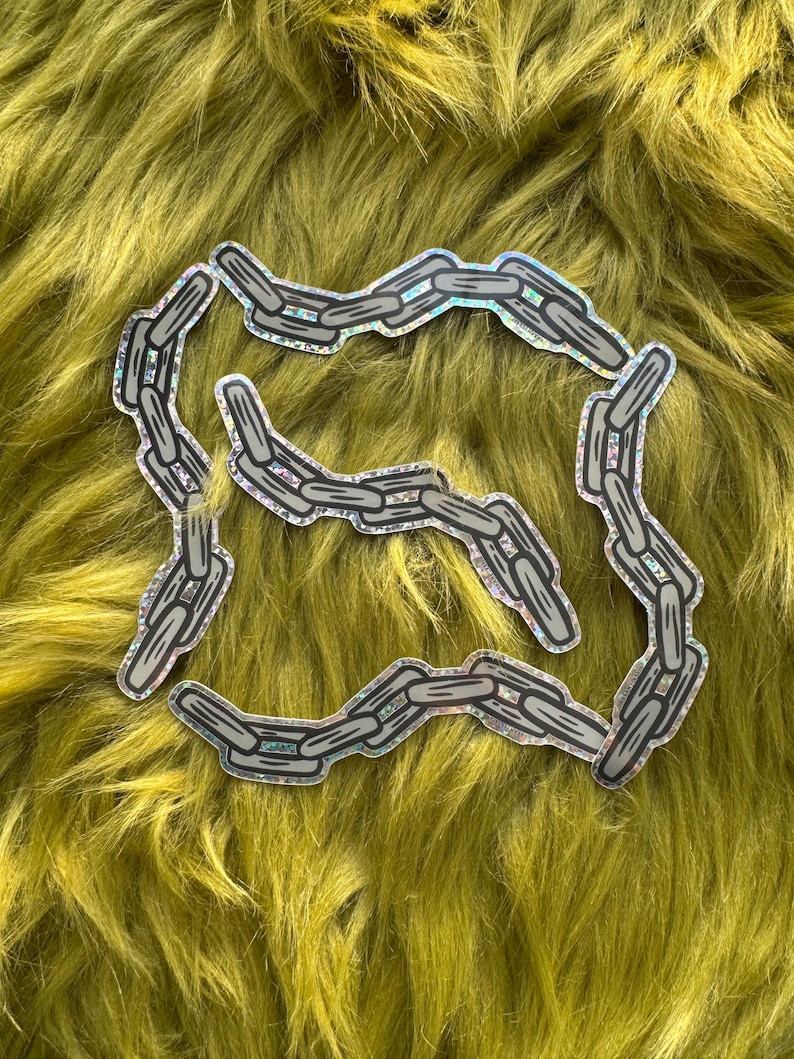 Puede incluir: Una pegatina de cadena plateada con acabado hologr&aacute;fico. La pegatina tiene forma de eslab&oacute;n de cadena y est&aacute; sobre un fondo verde peludo.