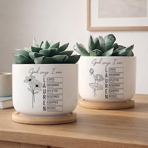 May include: Two white ceramic plant pots with succulents, each on a bamboo coaster. The pots feature the text "God says I am" and the name "LAUREN" with a list of positive affirmations. One pot has daisy graphics, the other has a lotus flower.