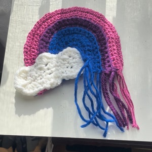 May include: A crocheted rainbow with a white cloud and blue, purple, and pink fringe.
