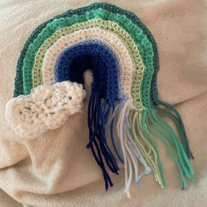 May include: A crocheted rainbow with a white cloud and blue, green, and white fringe.