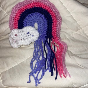 May include: A crocheted rainbow with a white cloud and pink, purple, blue, and dark blue yarn tassels.