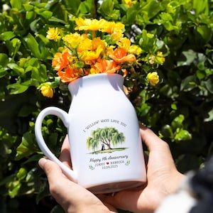 May include: White ceramic vase with a handle, filled with yellow and orange flowers. The vase has a printed design with a willow tree, two figures, and the text "I Willow Ways Love You". Below the tree is "Happy 9th Anniversary" and names and a date.