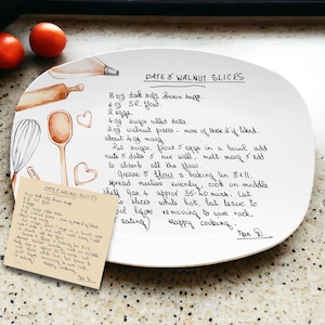 May include: A white ceramic plate with a handwritten recipe for walnut slices. The recipe includes ingredients like brown sugar, flour, eggs, dates, and walnuts. The plate is decorated with watercolor illustrations of kitchen tools and hearts.