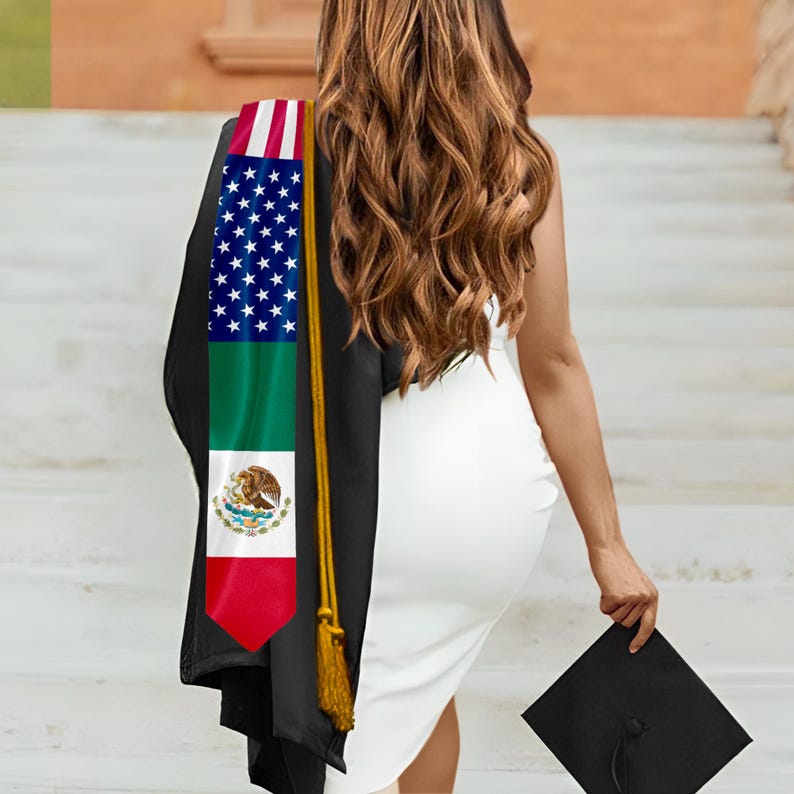 Puede incluir: Una banda de graduaci&oacute;n con las banderas estadounidense y mexicana, sobre una toga de graduaci&oacute;n negra. La banda es roja, blanca, azul y verde. Un birrete negro se sostiene en la mano. La persona lleva un vestido blanco.