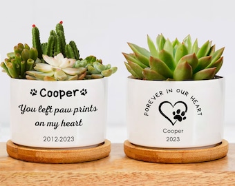 May include: Two white ceramic succulent planters with personalized messages. The left planter says "Cooper You left paw prints on my heart 2012-2023". The right planter says "Forever in our heart Cooper 2023".
