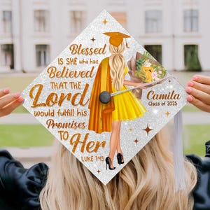 May include: A diamond-shaped graduation cap topper with a silver glitter finish. It features an illustration of a person with long blonde hair wearing a yellow dress, a graduation cap, and a gown, holding a bouquet. Text reads: Blessed IS SHE who has Believed THAT THE Lord would fulfill his Promises TO Her LUKE 1:45 Camila Class of 2025.