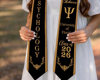 May include: Black and gold Psychology graduation sash with the text "PSYCHOLOGY" vertically. The sash also includes the name "Taylor Rebecca", the Greek letter Psi, "University of Florida", and "Class of 2026".