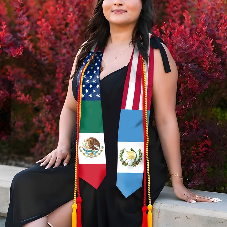 Puede incluir: Un vestido negro con estolas de graduaci&oacute;n con las banderas de Estados Unidos, M&eacute;xico y Guatemala. Las estolas tienen borlas doradas y rojas. El fondo es un arbusto rojo vibrante.