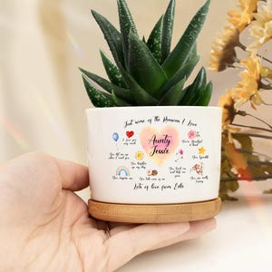 May include: White ceramic planter with a heart-shaped design that says "Just some of the reasons I love Aunty Jessie" with a list of reasons below. The planter has a bamboo base and is holding a small green succulent plant.