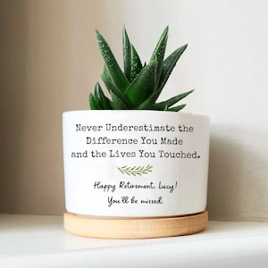 May include: White ceramic planter with a green succulent plant. The planter has the text "Never Underestimate the Difference You Made and the Lives You Touched. Happy Retirement, Lucy! You'll be missed." printed on it.