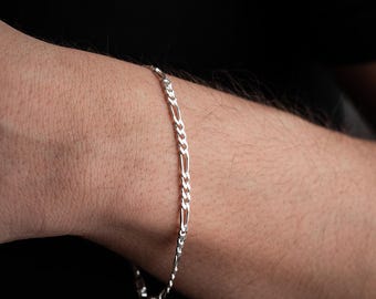 May include: A silver chain bracelet with a figaro link pattern.