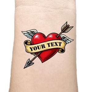 Puede incluir: Un corazón rojo con alas y una flecha que lo atraviesa. Una pancarta con el texto "YOUR TEXT" envuelve el corazón. El diseño recuerda a un tatuaje clásico.