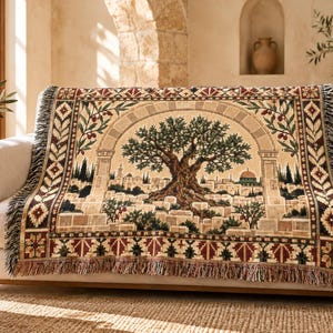 May include: A woven throw blanket featuring a detailed tapestry design of an ancient olive tree centered within a stone archway, overlooking a cityscape with a domed building. The border displays geometric patterns in shades of red, green, and tan.