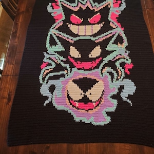 May include: A black crochet blanket with a colorful image of three ghost-like Pokemon characters. The characters are Gengar, Haunter, and Gastly. The blanket is made with a variety of colors, including pink, purple, blue, and green.