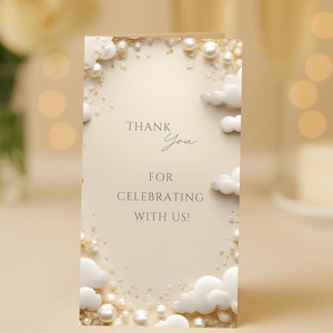 Könnte beinhalten: Eine cremefarbene Dankeskarte mit dem Text "Thank You For Celebrating With Us!" in eleganter Schrift. Die Karte ist mit weißen Wolken, goldenem Glitzer und Perlenakzenten verziert und schafft ein festliches Design.