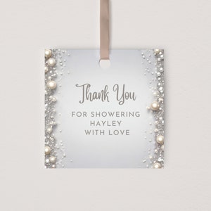 Puede incluir: Una etiqueta de agradecimiento blanca con purpurina plateada y detalles de perlas. La etiqueta dice "Gracias" por duchar a Hayley con amor.