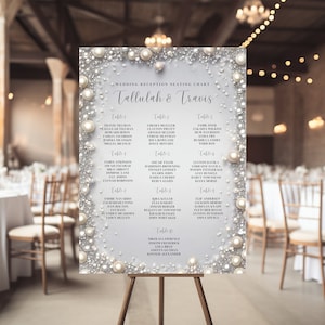Op de afbeelding: Een zitplaatskaart voor een huwelijksreceptie met een parel- en zilveren glitterontwerp. De kaart vermeldt de namen van de gasten die aan elke tafel zijn toegewezen. De kaart heeft de titel "Wedding Reception Seating Chart Tallulah & Travis".