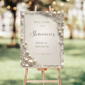 Puede incluir: Un cartel de bienvenida blanco con un borde de perlas. El cartel dice "Bienvenido a Shannon's Bridal Shower 26 de octubre de 2021".
