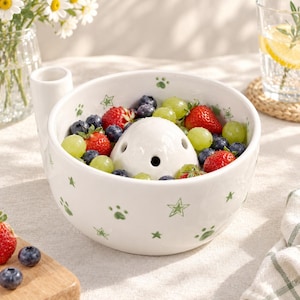Pode incluir: Uma taça de cerâmica branca para frutos silvestres com uma pequena pega vertical e uma cúpula central com orifícios de drenagem. O exterior e o interior estão decorados com pequenas estrelas e pegadas verdes, cheia de fruta fresca.